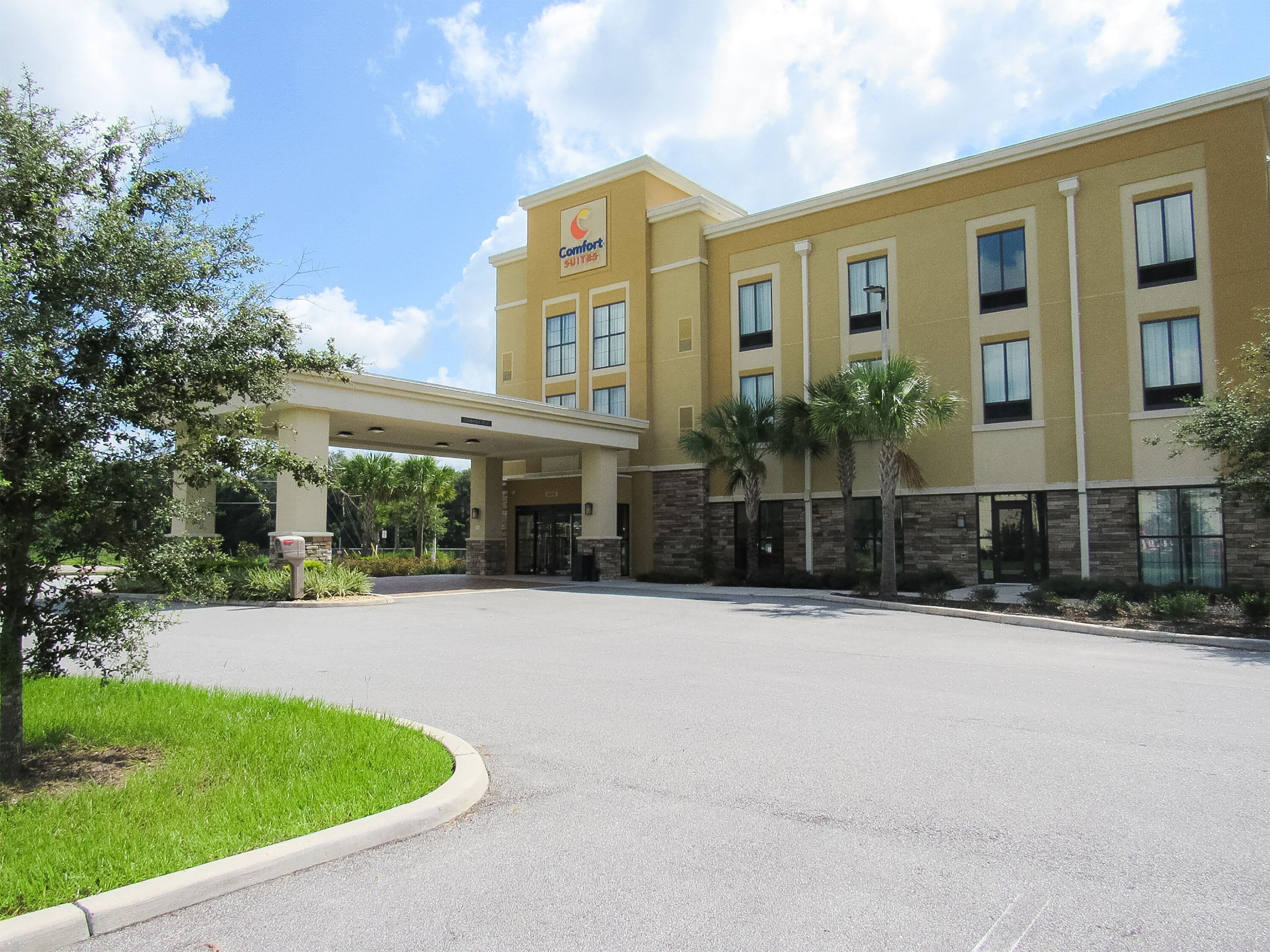Un hotel Comfort Suites con entrada techada, palmeras y cielo despejado.