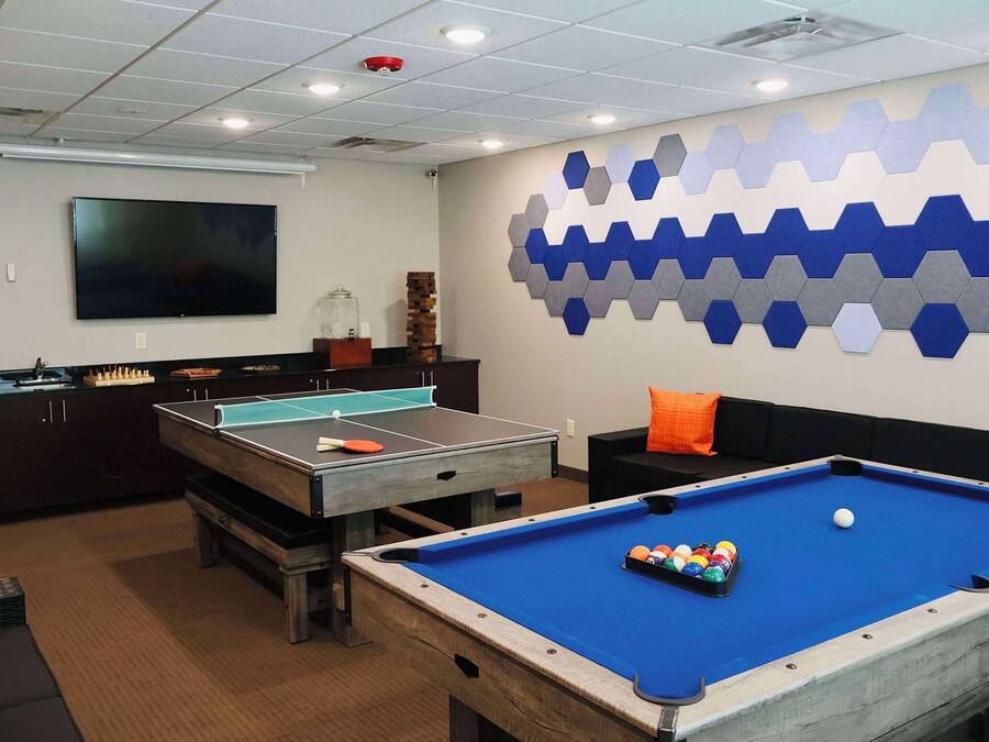 Una mesa de billar con bolas, una mesa de ping pong y un televisor de pantalla plana en una habitación con diseño de pared hexagonal.