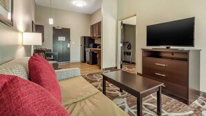 Una sala de estar moderna con sofá, mesa de centro, televisor y una cocina al fondo.
