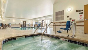 Una piscina interior con agua cristalina, una silla de salvavidas y una zona junto a la piscina con sillas y mesas.