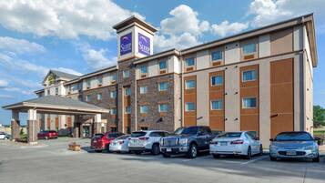 A hotel with a modern design, featuring a central entrance, multiple parking spaces, and a clear sky.