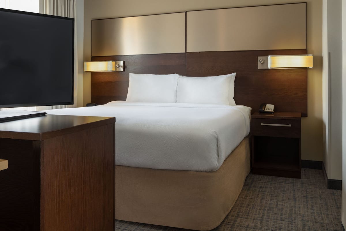 Ein Hotelzimmer mit einem großen Bett, einem Fernseher, einem Nachttisch und einem Beistelltisch.