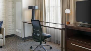 Een hotelkamer met een bureau, stoel, televisie, lamp en uitzicht op het omliggende landschap.