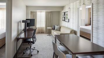 A hotel room with a desk, office chair, sofa, and a small round table.