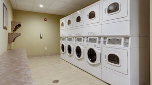 A laundry room with multiple stacked washing machines and dryers, a tiled floor, and a light-colored wall.
