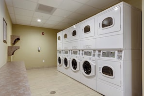 A laundry room with multiple stacked washing machines and dryers, a tiled floor, and a light-colored wall.