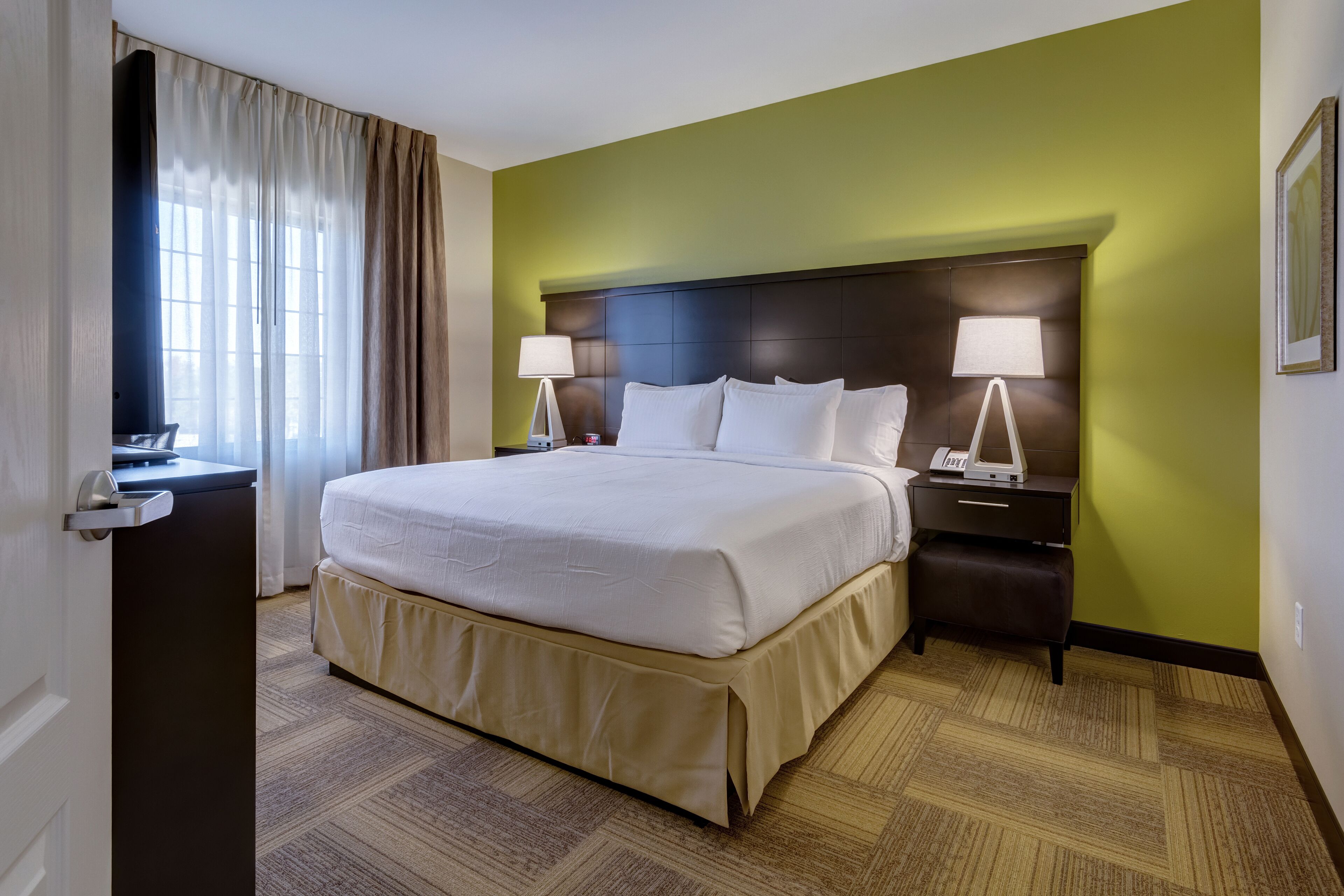 Une chambre d’hôtel avec un grand lit, deux tables de chevet avec des lampes, un bureau et une fenêtre avec des rideaux.