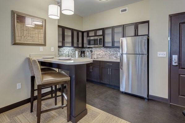 A modern kitchen with dark cabinets, stainless steel appliances, and a bar area. - Staybridge Suites St Louis - Westport by IHG (Maryland Heights)