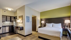 Habitación de hotel con cama, mesitas de noche, escritorio, silla, pequeña mesa, refrigerador, microondas, lavamanos y un armario.