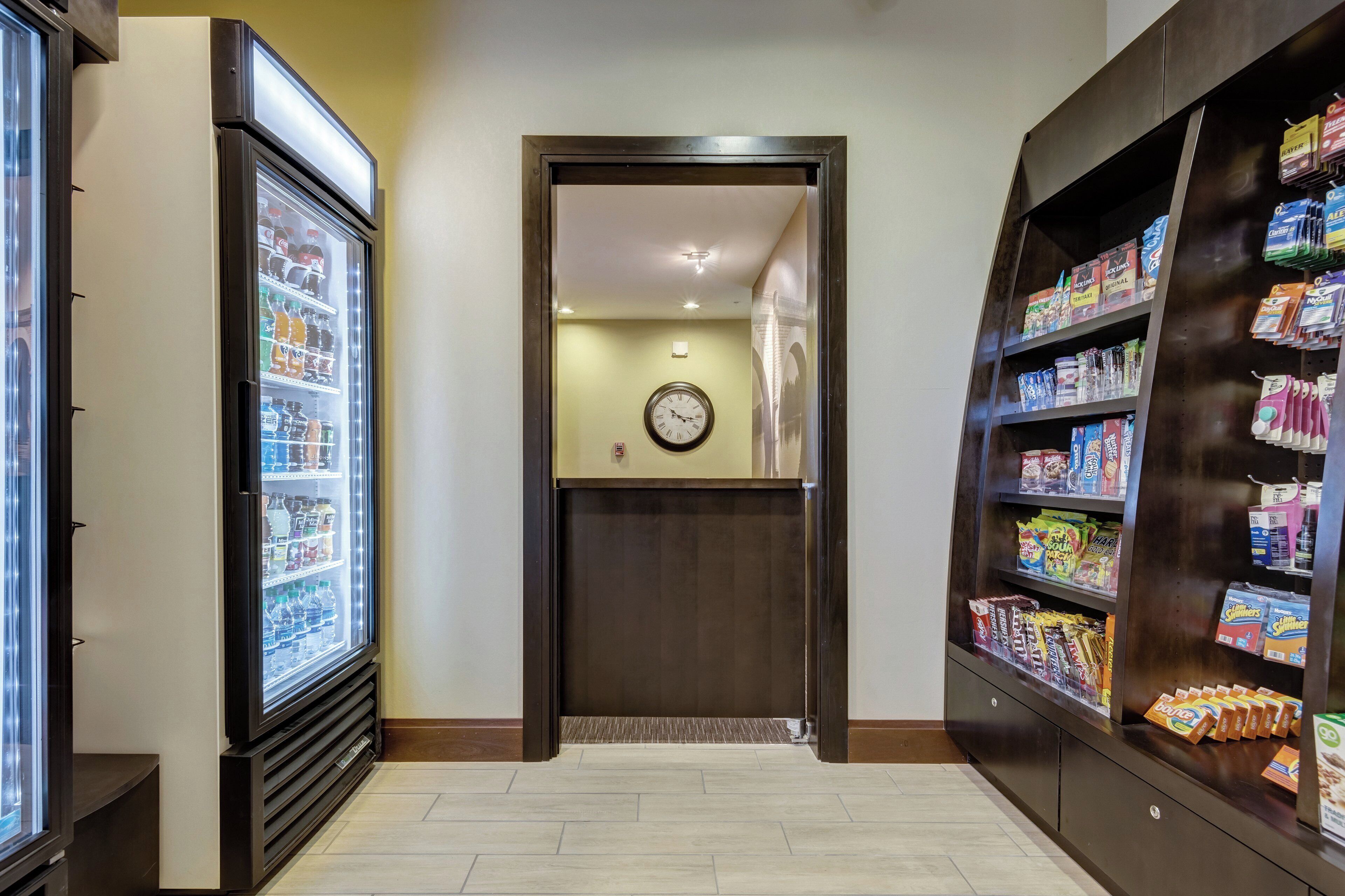 A hallway with a refrigerator, a clock, and a snack display.