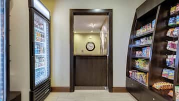 A hallway with a refrigerator, a clock, and a snack display.