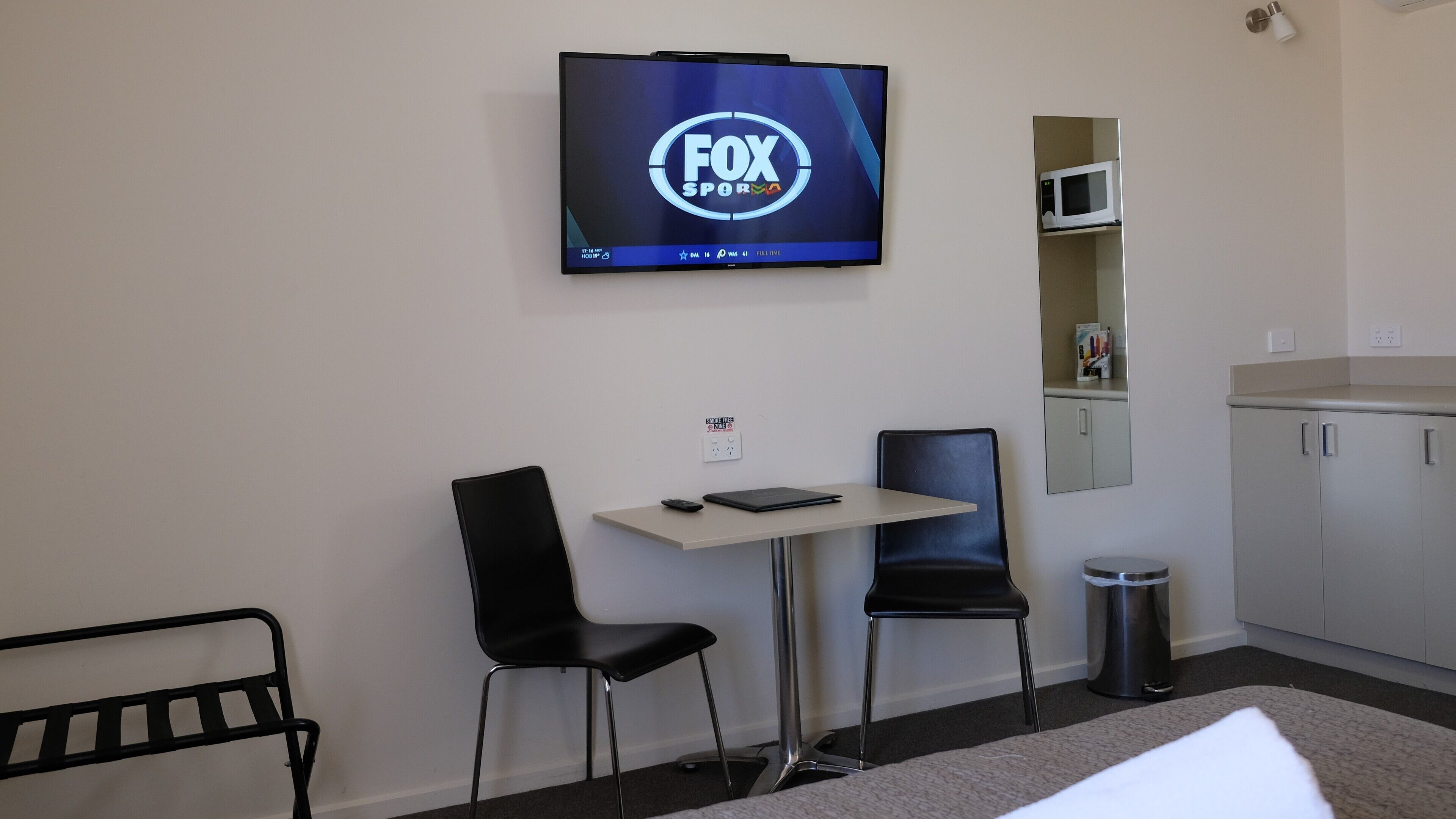 Habitación de hotel con una televisión mostrando FOX SPORTS, un escritorio con silla, un cesto de basura y una cama.