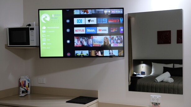 A hotel room with a flat-screen TV mounted on the wall displaying various TV channels and apps. - Loddon River Motel (Kerang)