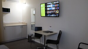 A small kitchenette with a microwave, a sink, and a cabinet. There is a table with two chairs and a tablet on it. - Loddon River Motel (Kerang)