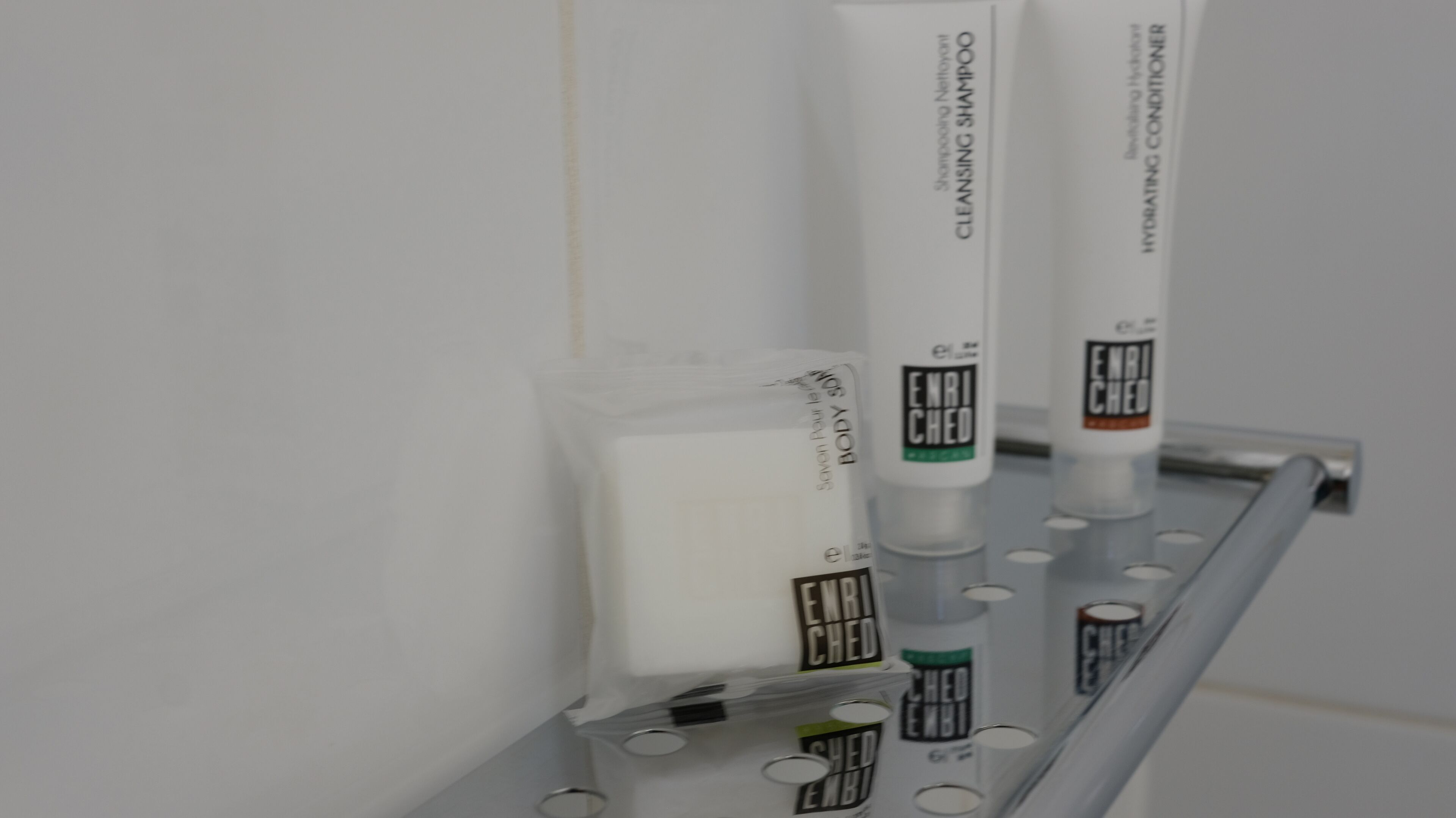 A row of toiletries on a metal shelf against a white wall.