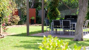 An outdoor patio area with a table and chairs, surrounded by greenery and a fence. - Loddon River Motel (Kerang)