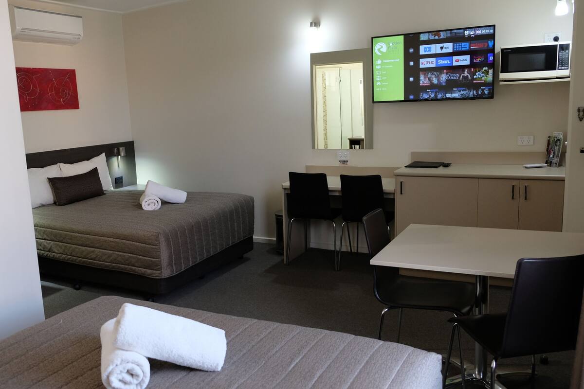 Una habitación de hotel con cama, escritorio, silla, televisor y microondas.