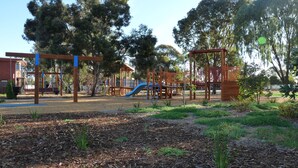 A playground with various play structures, including slides and swings, surrounded by trees and a grassy area. - Loddon River Motel (Kerang)