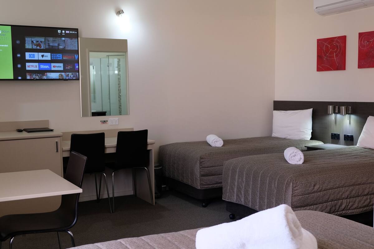 Habitación de hotel con escritorio, dos camas, televisor montado en la pared y microondas en la encimera.