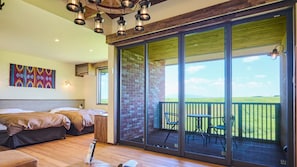 A bedroom with a large sliding glass door leading to an outdoor patio with a view of a green field. - El Patio Ranch (Aso)