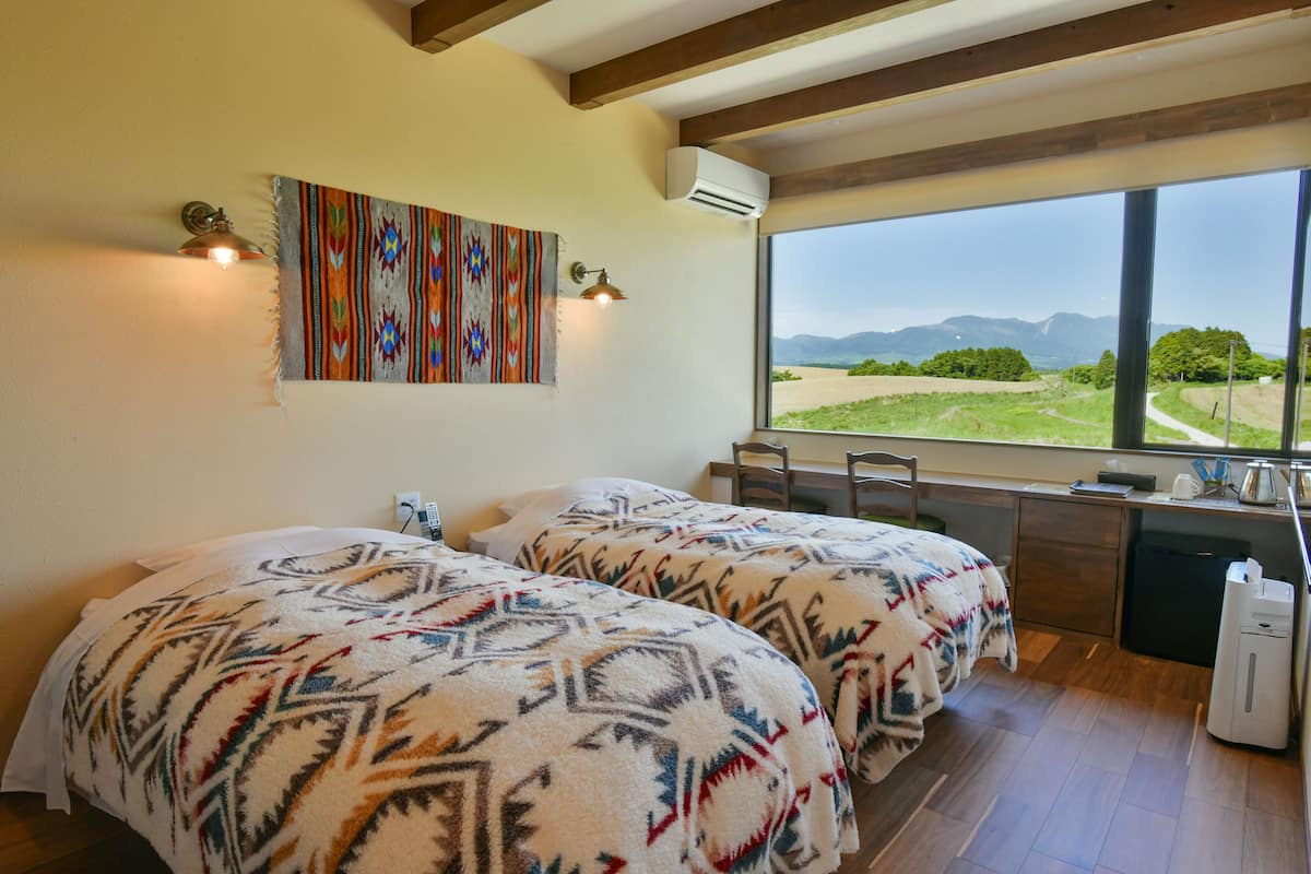 Una habitación con dos camas, un escritorio y un amplio ventanal con vistas al exterior.