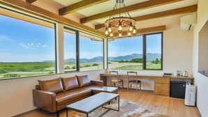 Una sala de estar moderna con un sofá de cuero, una mesa de centro y un amplio ventanal con vistas a un paisaje verde y montañas.