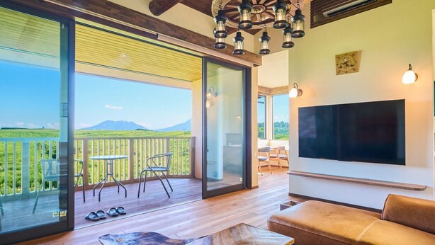 Un amplio espacio de sala con un televisor grande, piso de madera y un balcón con vista a la montaña.