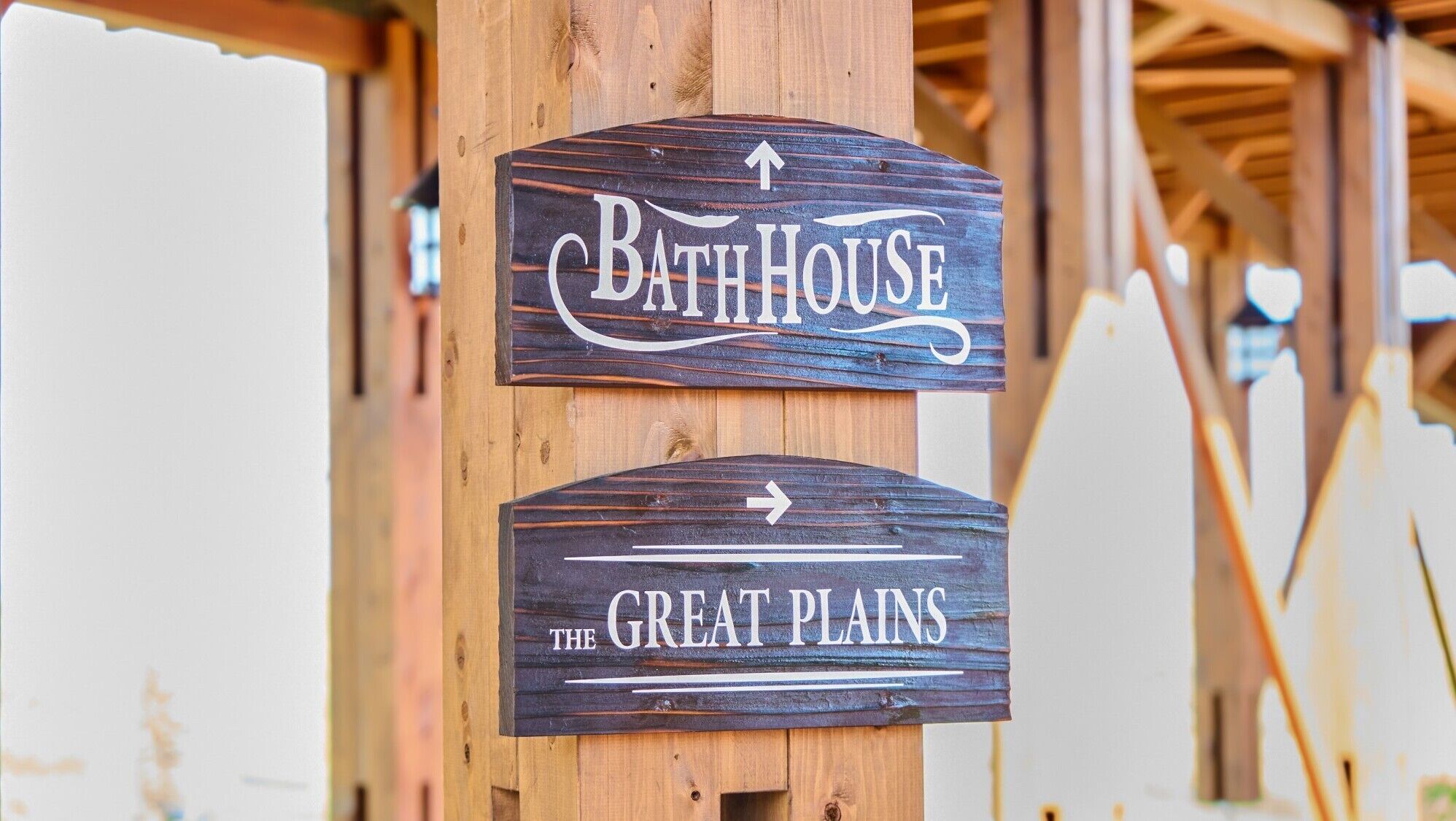 Un cartel de madera con dos señales direccionales: una apuntando hacia arriba con la leyenda 'BathHouse' y otra apuntando a la derecha con la leyenda 'The Great Plains'.