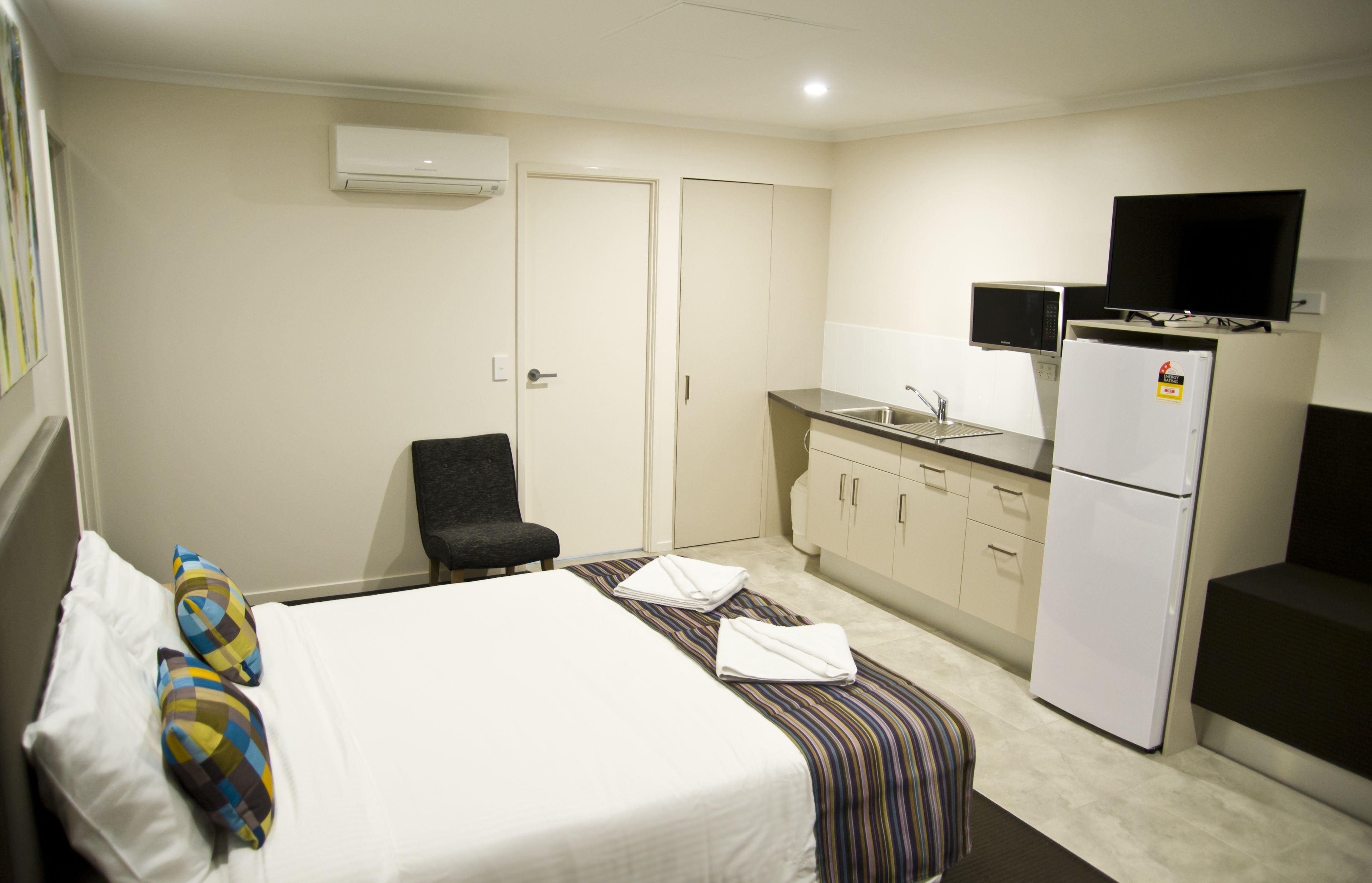 A hotel room with a bed, a chair, a small kitchenette with a microwave, a refrigerator, and a television.