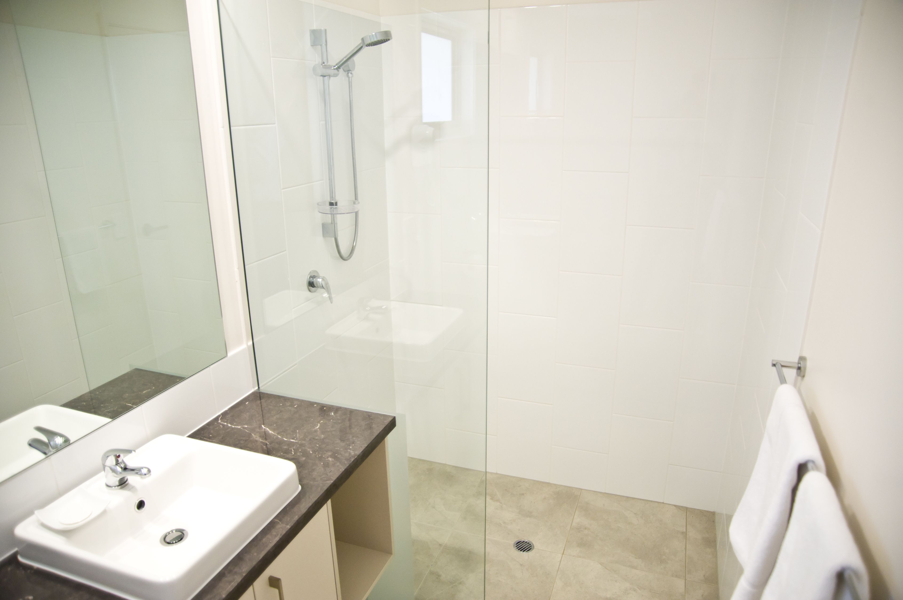 A modern bathroom with a glass-enclosed shower, a white sink, and a marble countertop.