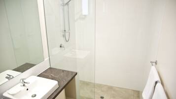 Un baño moderno con ducha de vidrio, lavamanos blanco y encimera de mármol.