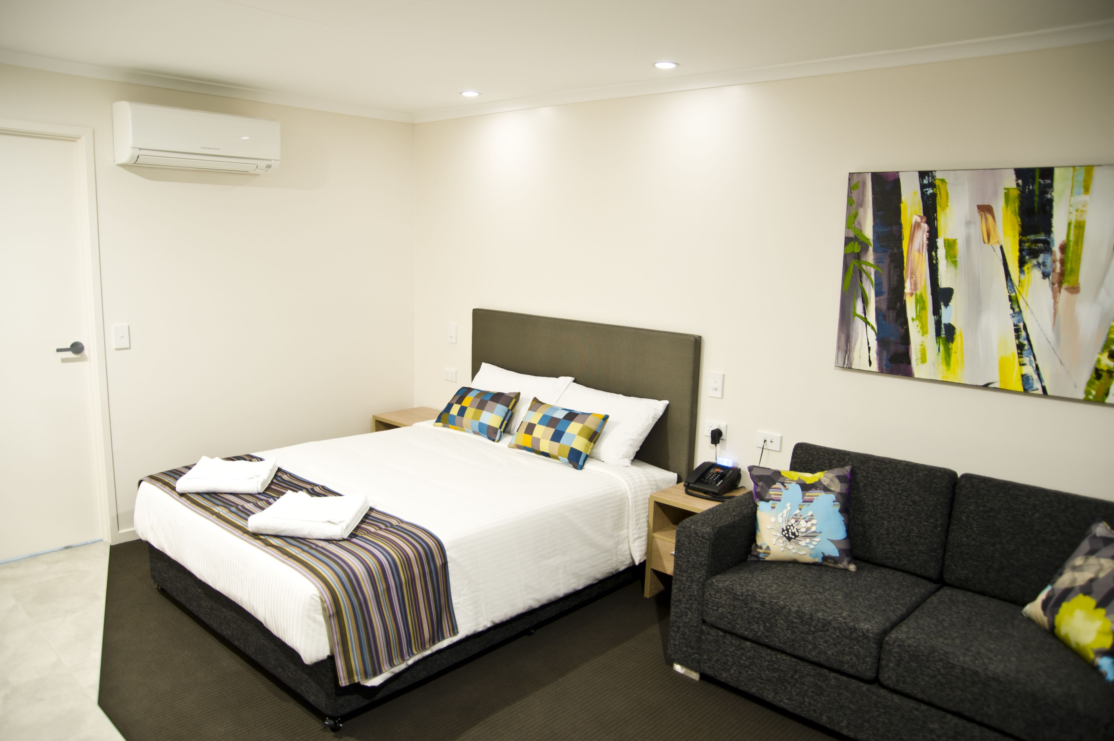Una habitación de hotel con una cama grande, un sofá gris, un cuadro en la pared y un equipo de aire acondicionado.