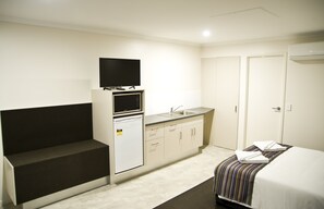 A compact hotel room with a bed, a small kitchenette, a flat-screen TV, and a private bathroom.