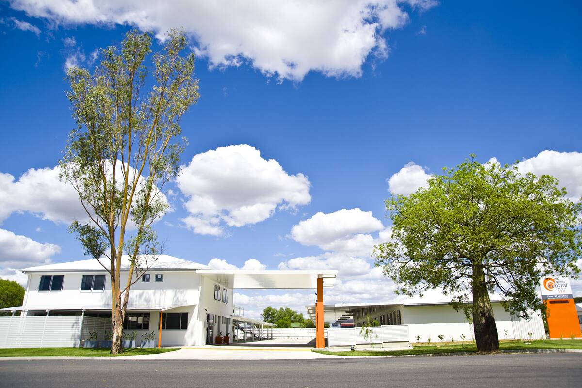 A modern building with a covered parking area, a large tree, and a clear blue sky.
