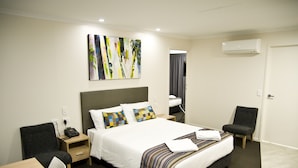 A modern hotel room with a large bed, a desk, a chair, and a painting on the wall.