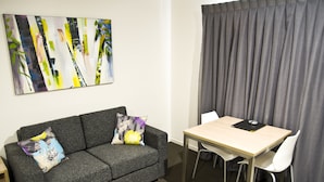 A modern room with a grey sofa, two patterned pillows, a wooden table with a black folder, and a grey curtain.
