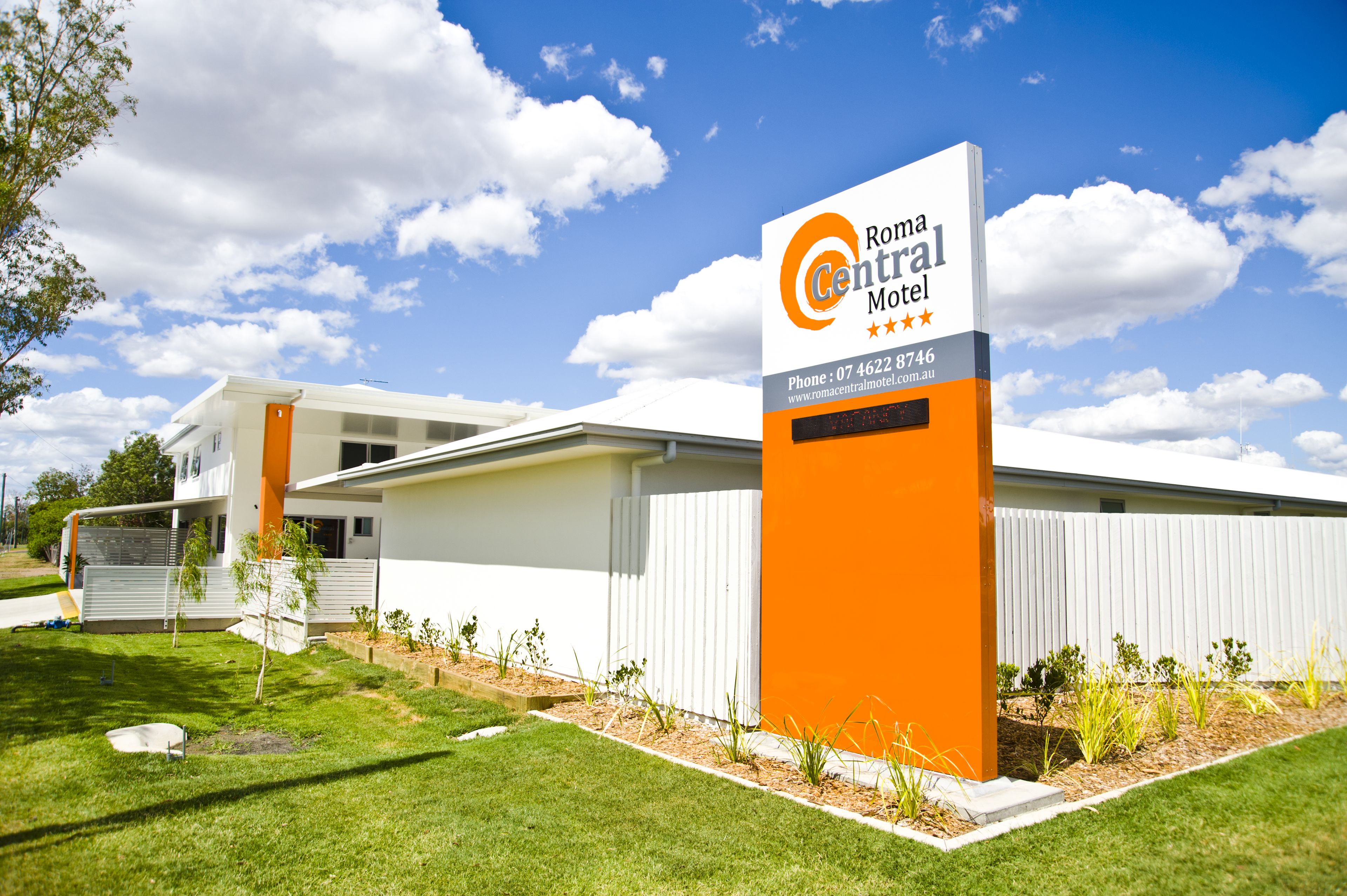 A modern hotel with a prominent orange and white sign, a well-maintained lawn, and a clear blue sky.