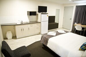 A hotel room with a bed, a desk, a chair, a kitchenette with a refrigerator and microwave, and a bathroom.