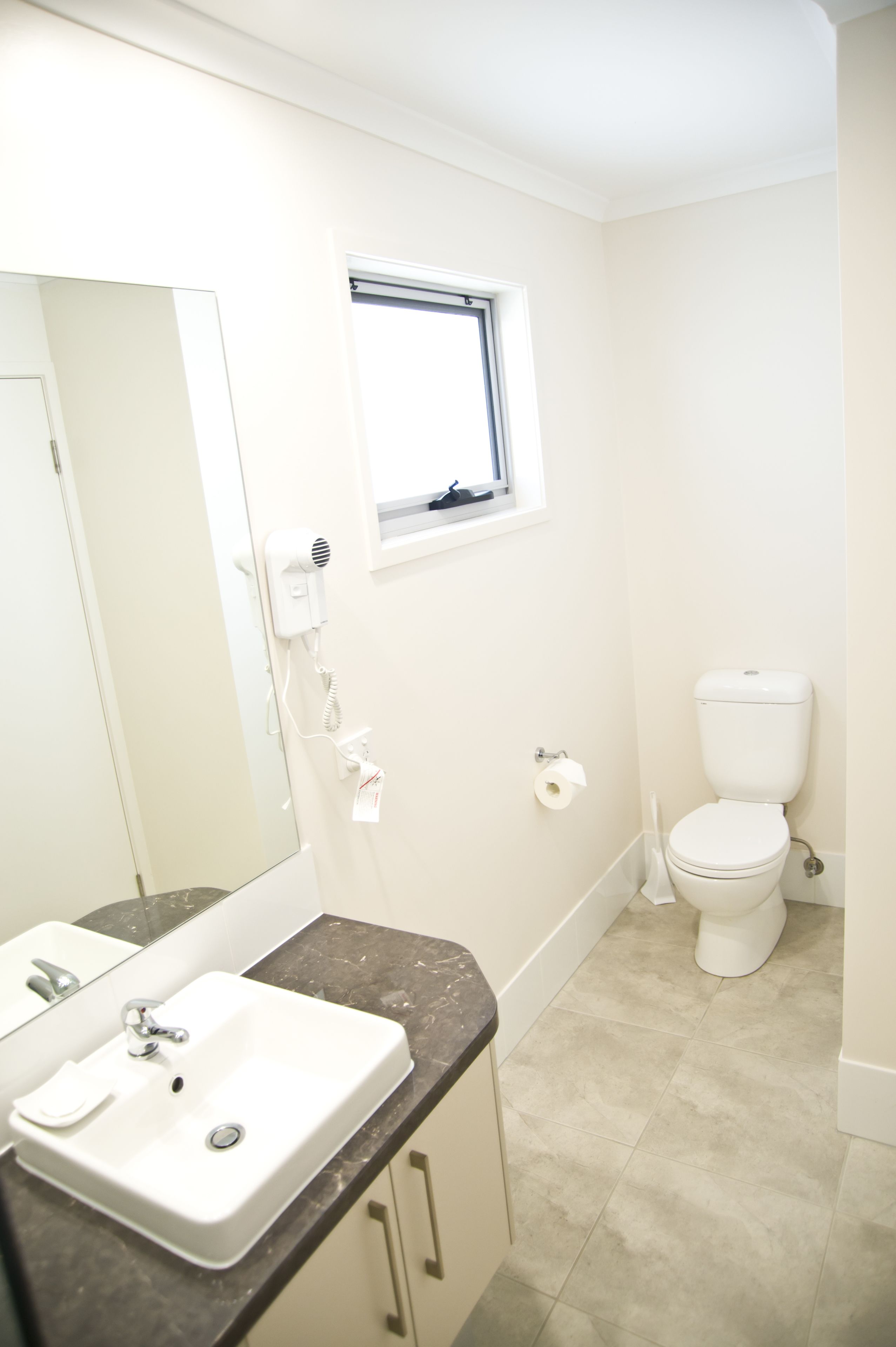 Een badkamer met een wit wastafelmeubel, een spiegel, een raam en een toilet.