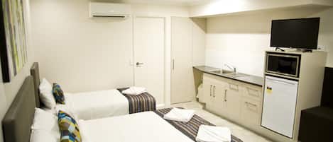 Une chambre d’hôtel avec deux lits, une kitchenette, un téléviseur et un appareil de climatisation.