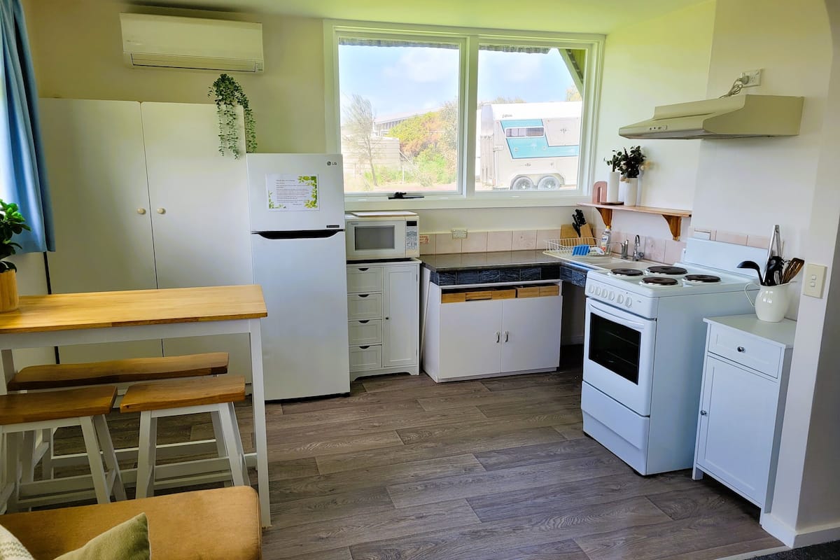A compact kitchen with white cabinetry, a microwave, a stove, and a dining area with wooden benches.