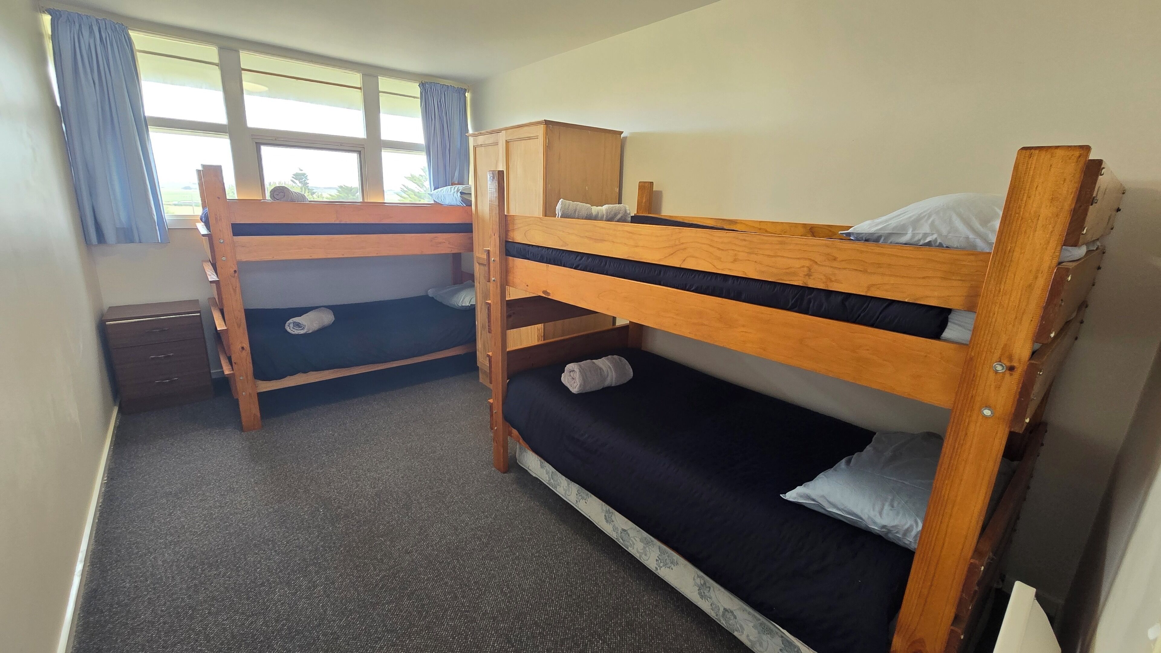 Une chambre de dortoir avec deux lits superposés, un bureau et une fenêtre avec des rideaux.