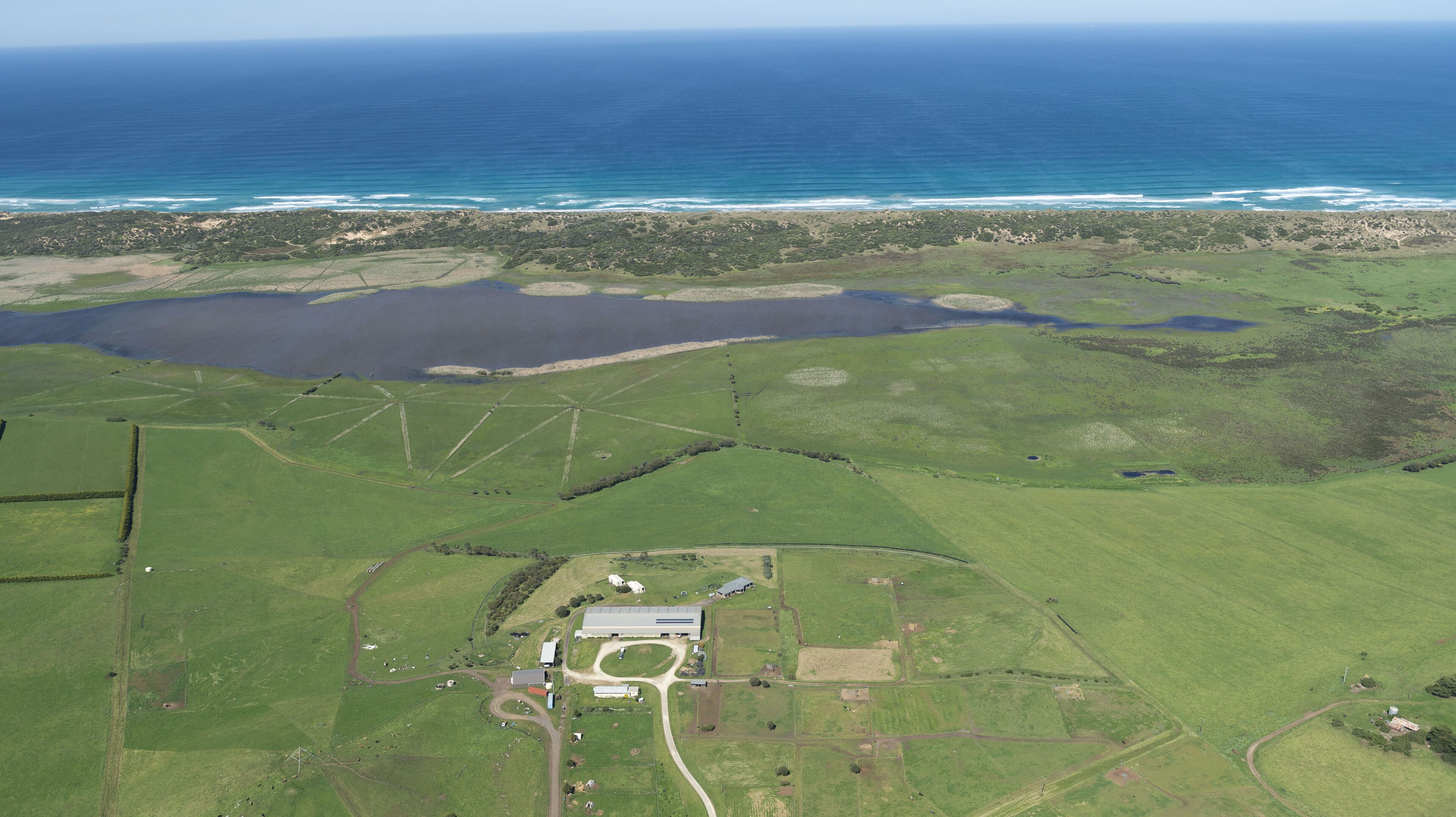 An aerial view of a rural property with fields, a large pond, and a building with a long driveway.