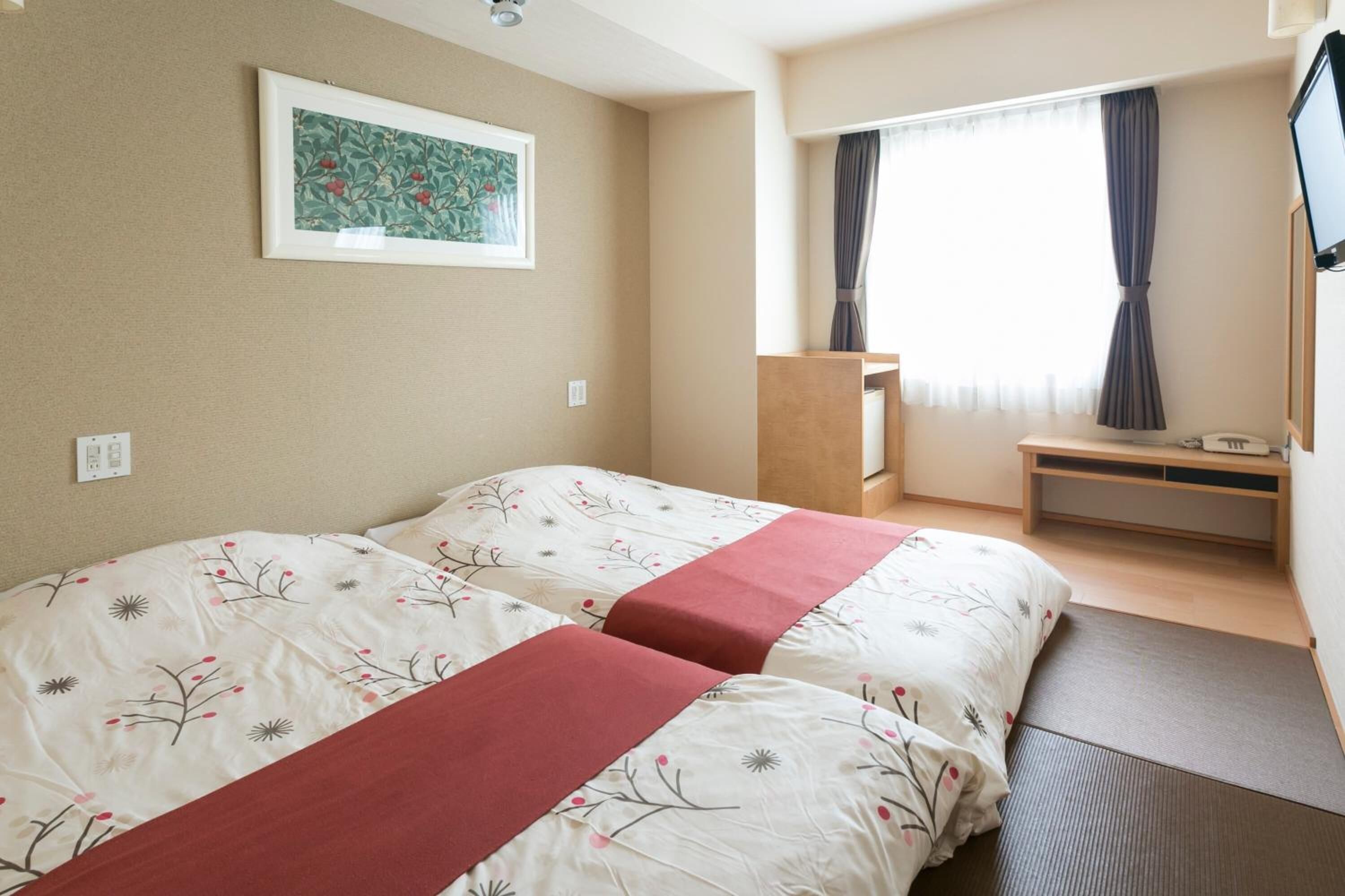 A hotel room with two beds, a desk, a chair, a TV, and a window with curtains.