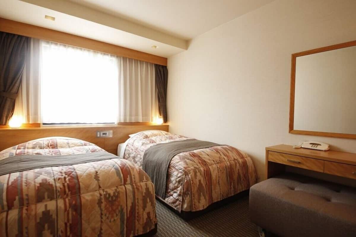 Una camera d'albergo con due letti, un comodino con un telefono e un grande specchio a parete.