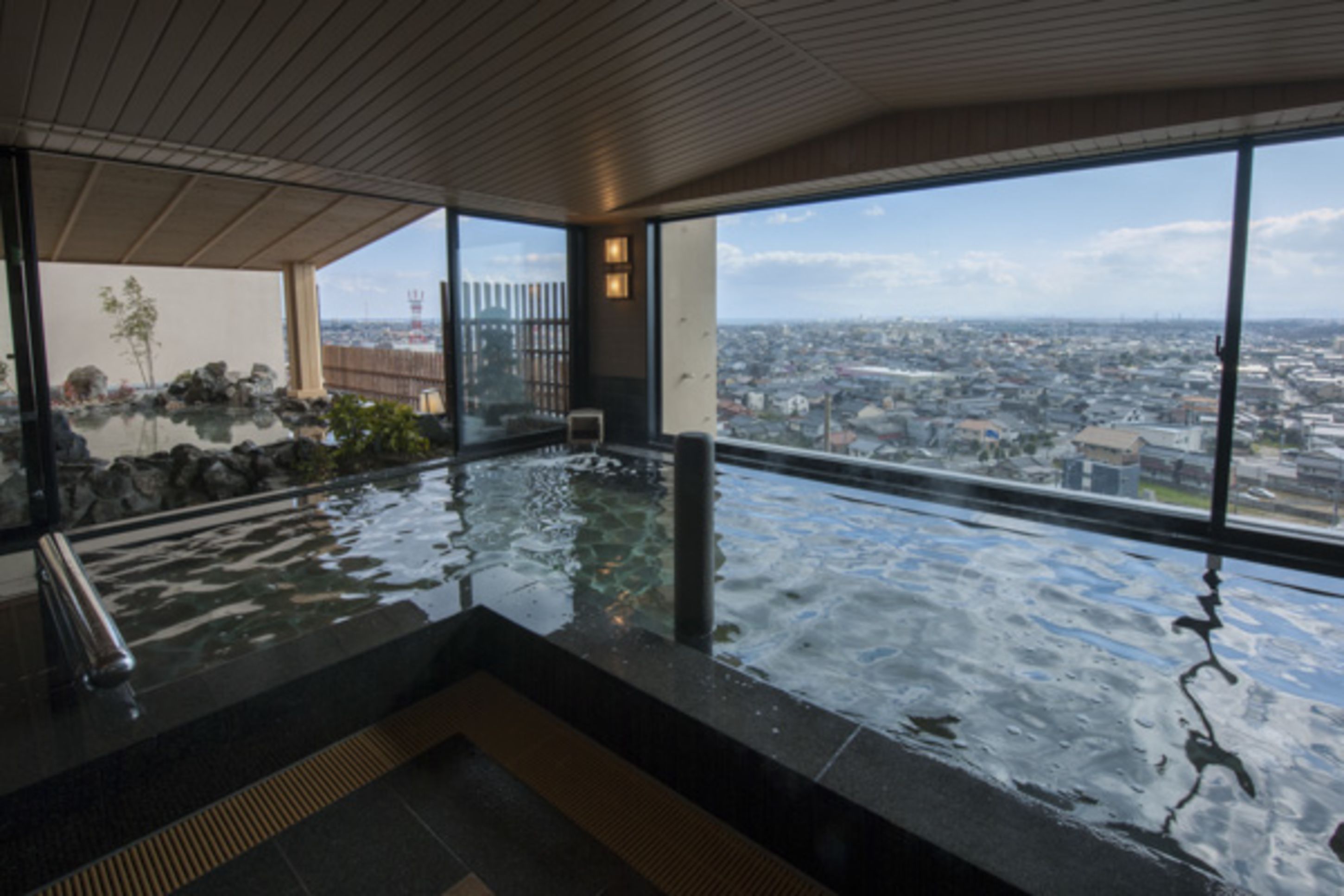 A modern indoor pool with a city view, large windows, and a wooden ceiling.