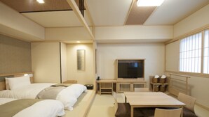 Et hotelværelse med to senge, fjernsyn, et spisebord og et stort vindue.