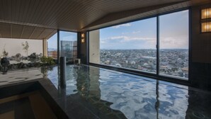 En moderne swimmingpool indendørs med udsigt over byen, store vinduer og et træloft.
