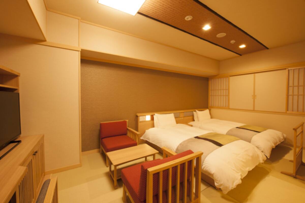 A hotel room with a bed, a TV, a desk, and a chair.