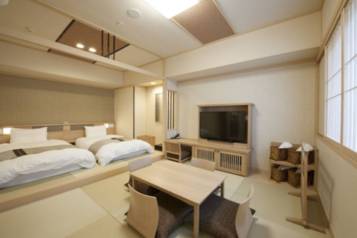 A hotel room with a large bed, a TV, a desk, and a window.